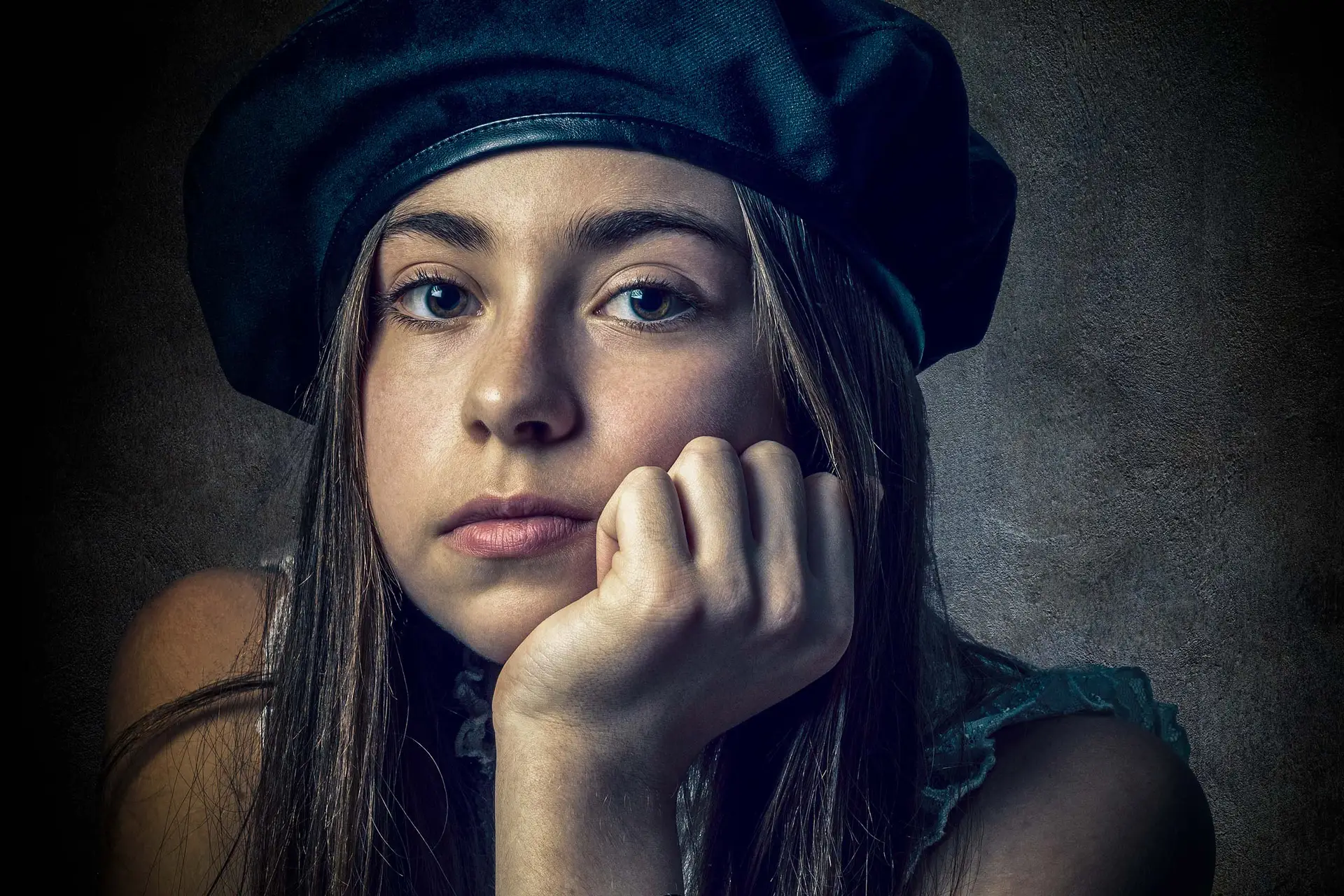 Young woman in a dark beret resting her chin on her hand in a dramatic, low-key studio portrait