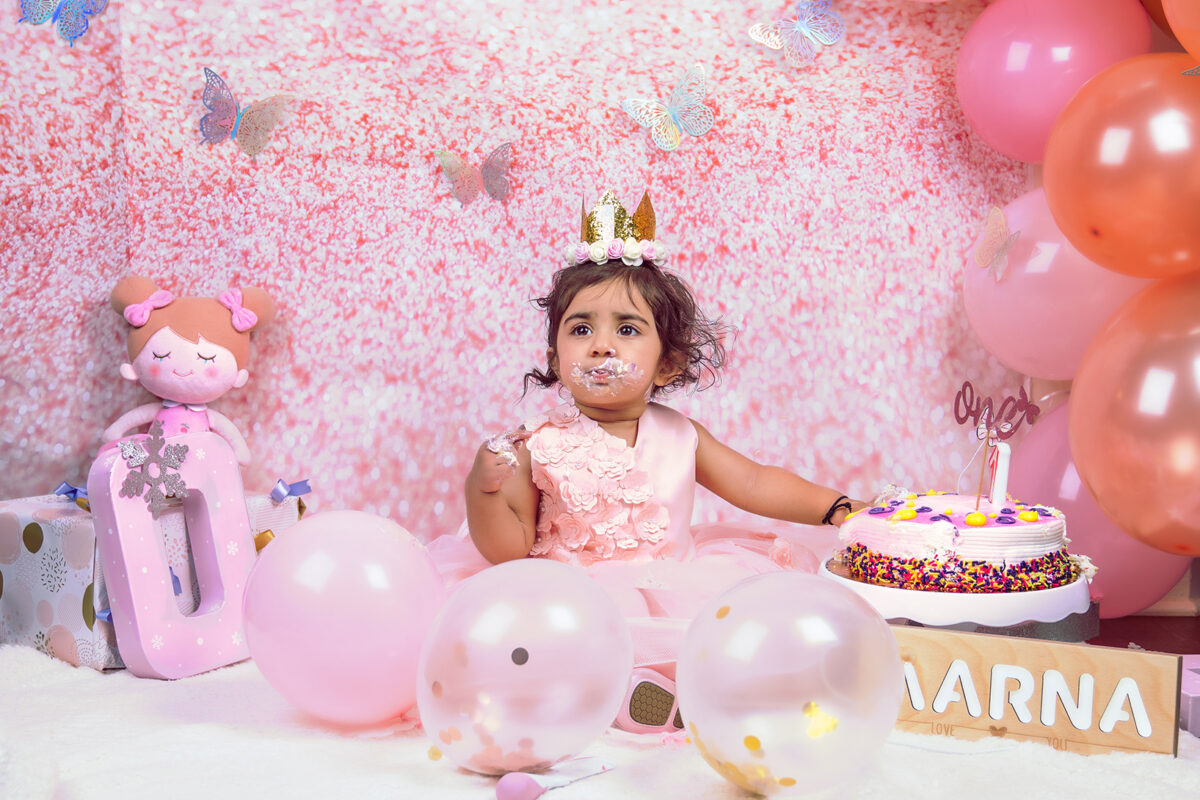 Little girl in a pink dress at her birthday balloon backdrop