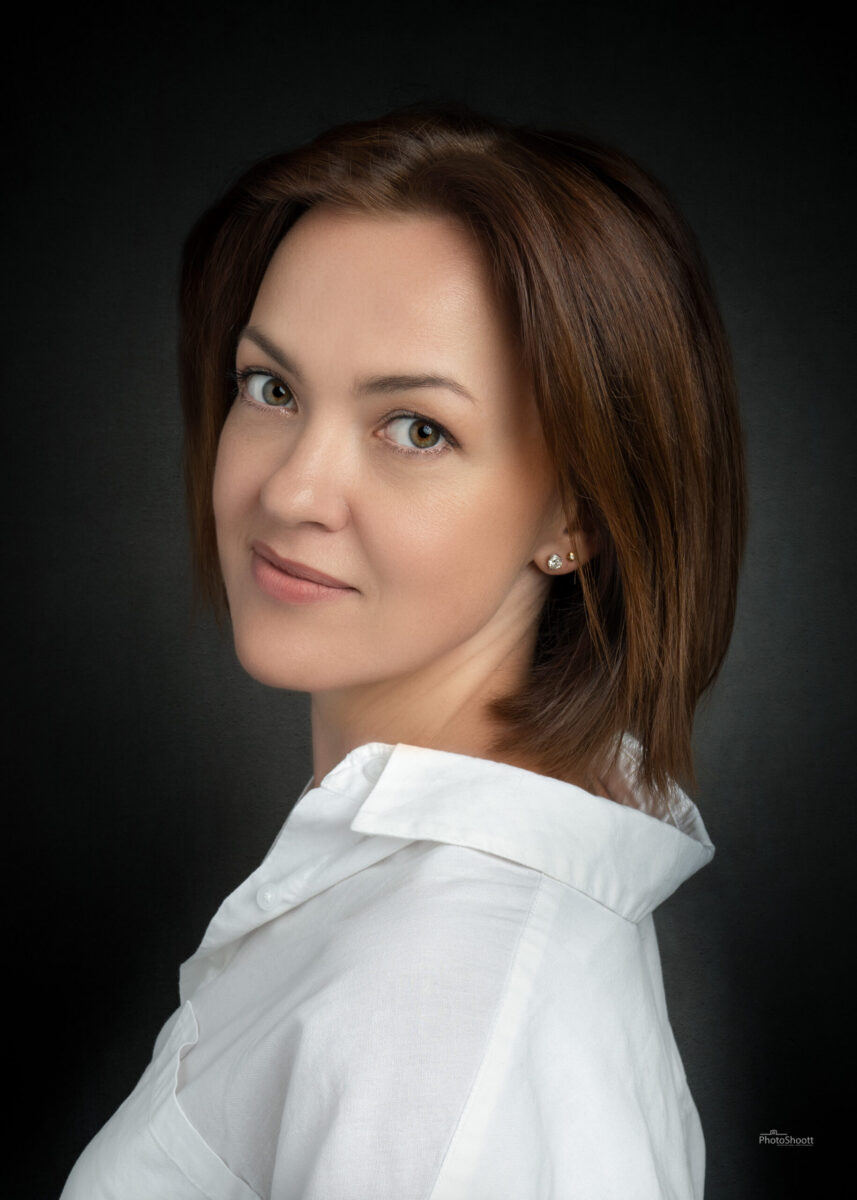 Woman with auburn hair in a soft studio headshot on a dark backdrop
