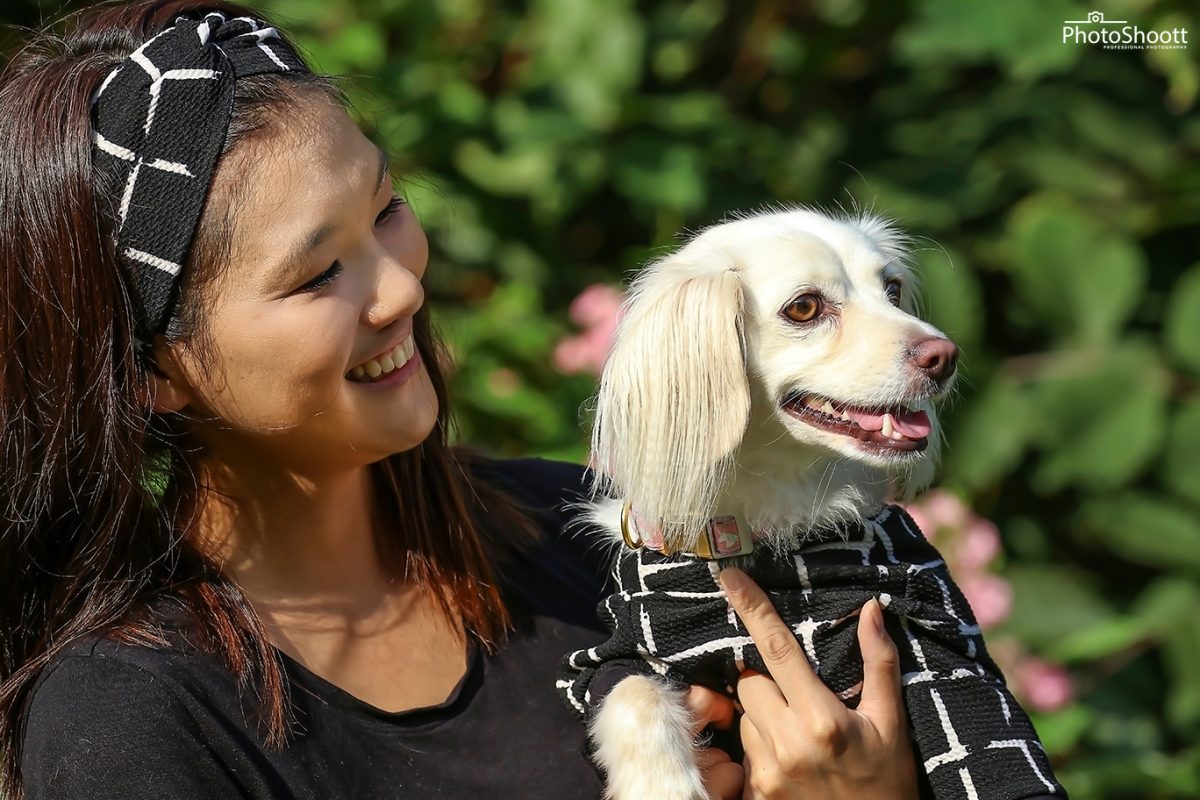 Smiling woman holding a small white fluffy dog in a matching outfit