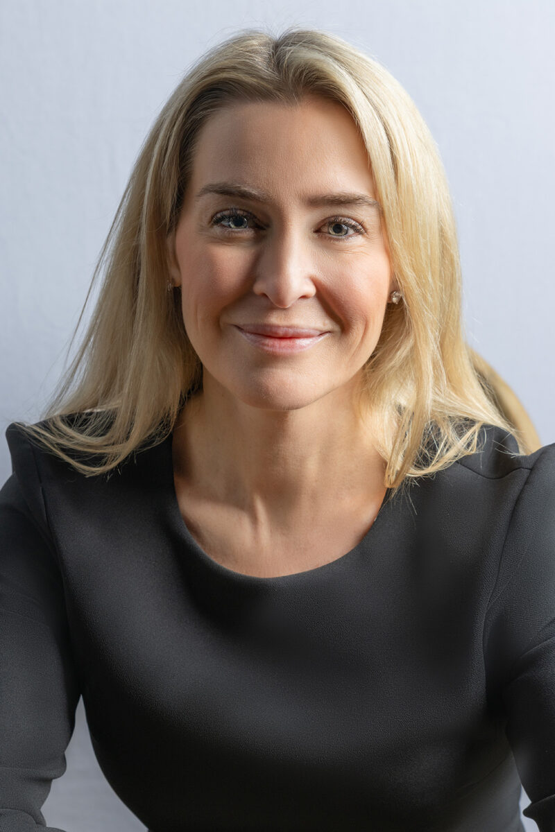 Smiling woman with blonde hair in a professional headshot against a grey backdrop