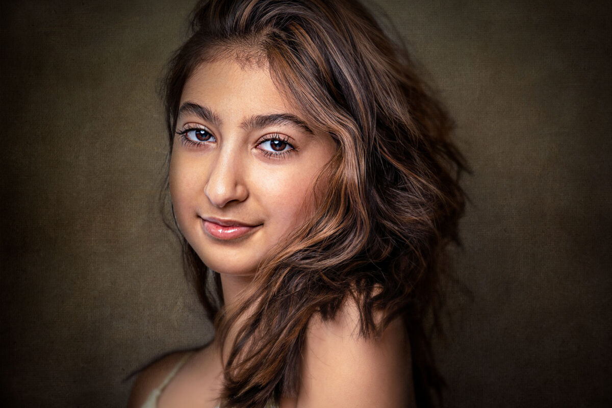 Teenage girl with long dark hair in a studio portrait on a black backdrop