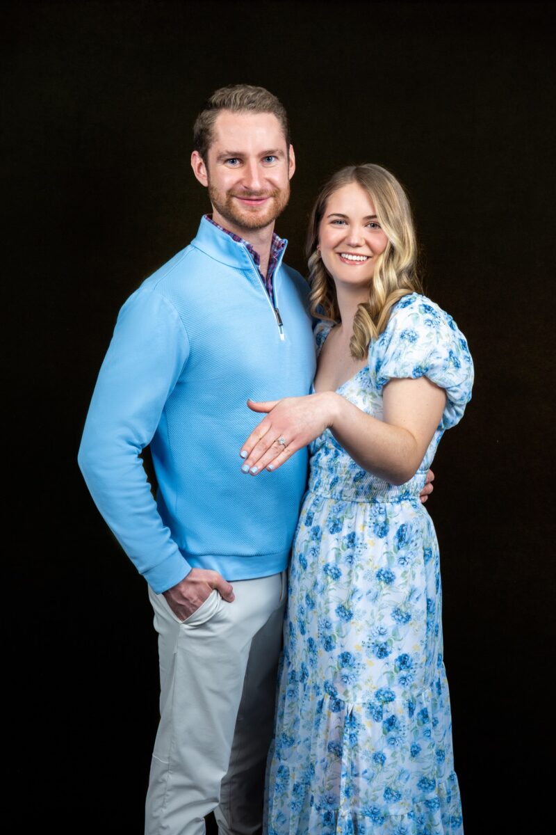Engaged couple Casey and Bobby posing together on a black studio backdrop