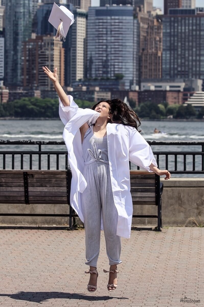 Graduate in a white gown celebrating by the water