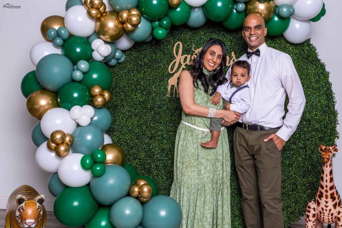 Family posing in front of a balloon arch at a first birthday party