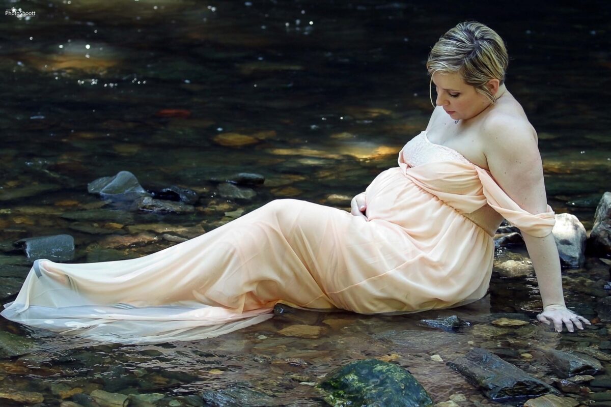 Expectant mother in a gown reclining beside a forest stream