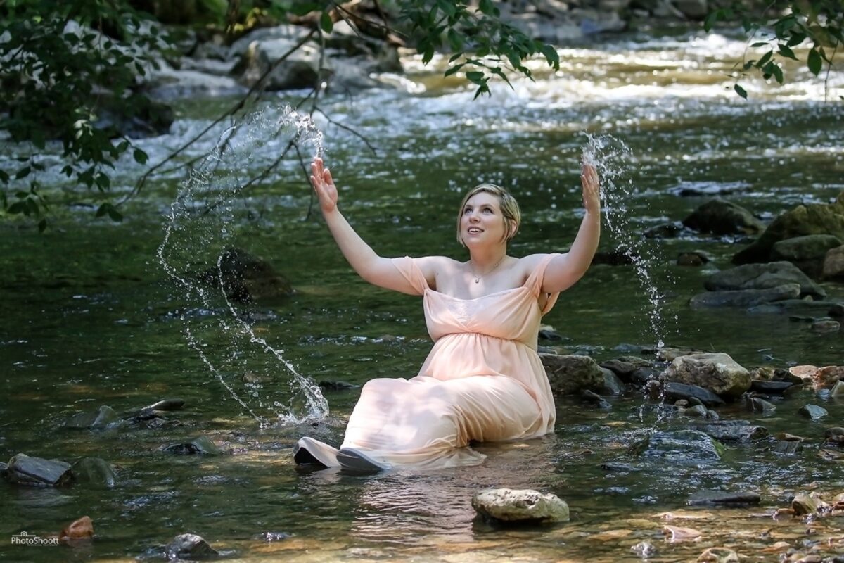Expectant mother splashing in a stream during a maternity session