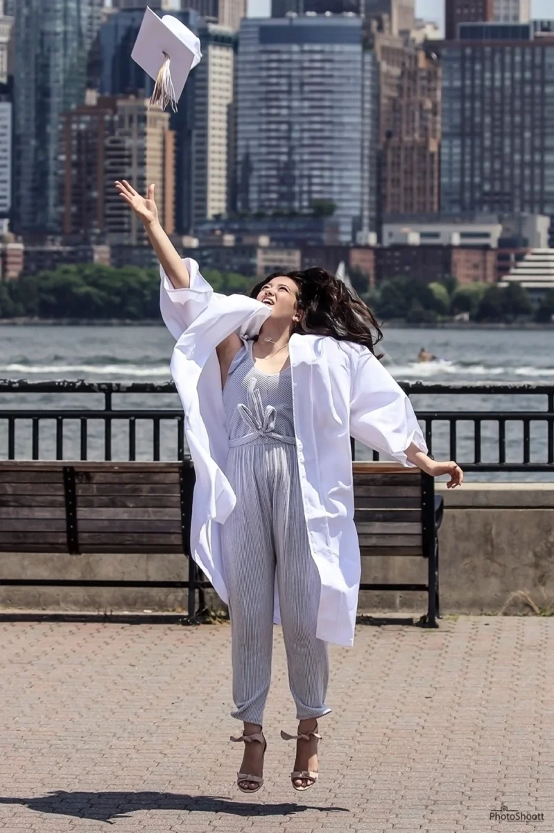 Graduate in a white gown celebrating by the water