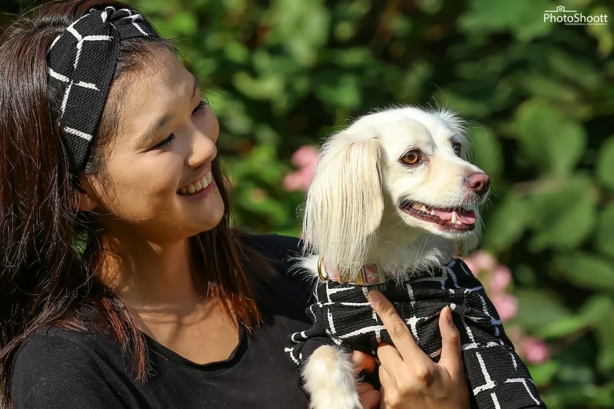 Smiling woman holding a small white fluffy dog in a matching outfit