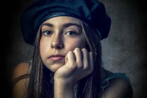 Young woman in a dark beret resting her chin on her hand in a dramatic, low-key studio portrait